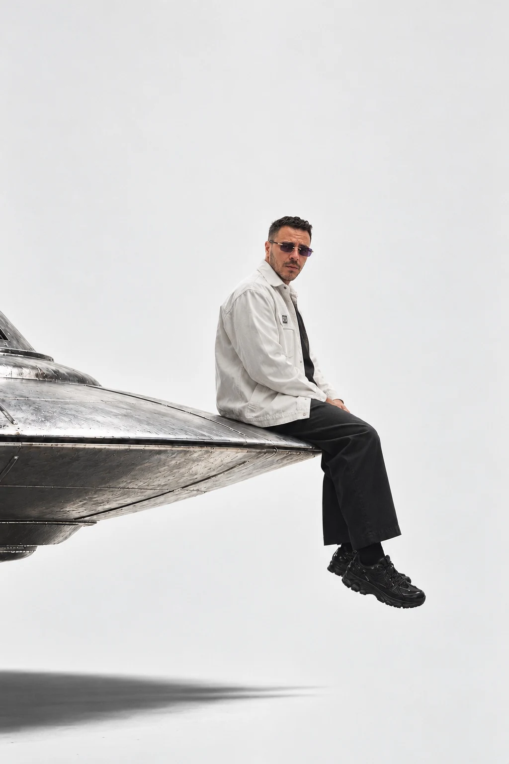 Sedat Erol Atamen in a white jacket and dark trousers, seated on a metallic aircraft body